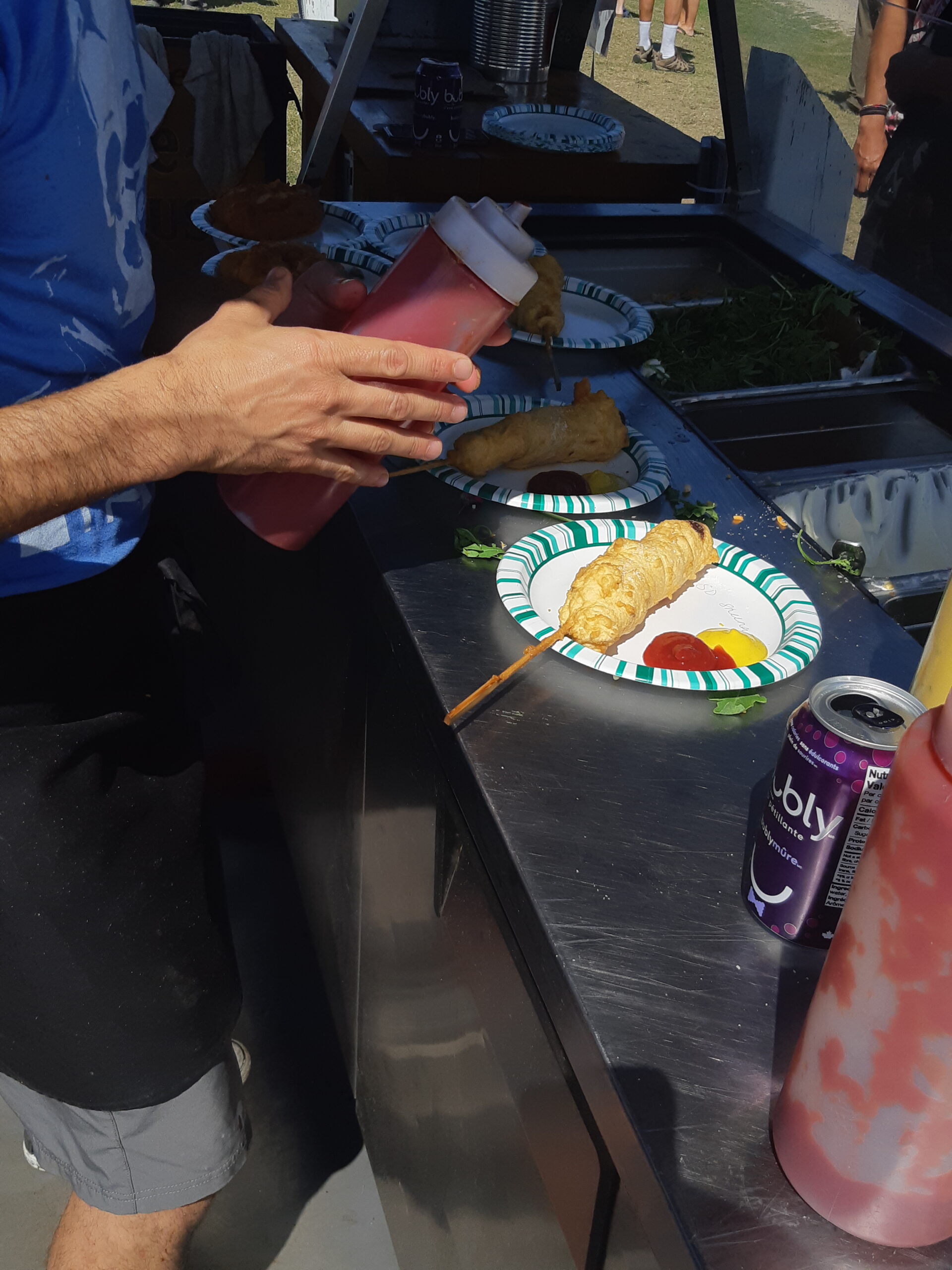 20220731_152918 People adding condiments to their food at an outdoor festival.