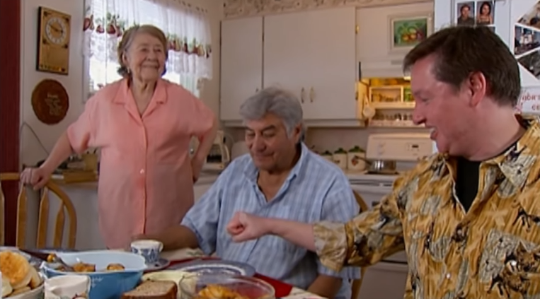 Screenshot 2025-12-02 190842 People sitting down to a meal in a small kitchen.