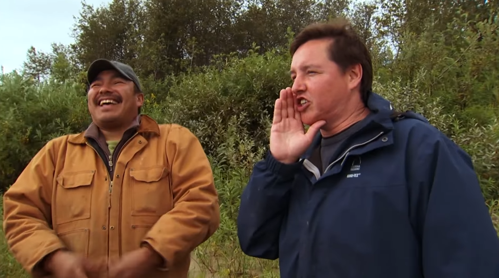 Screenshot 2025-12-02 191510 Two men having a conversation in the fall in front of some bushes.