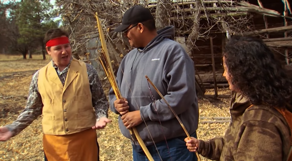 Screenshot 2025-12-02 192126 A group of people discussing archery while holding some bows and arrows.